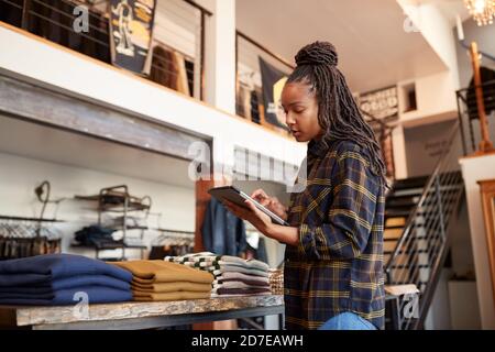 Donna proprietaria del Fashion Store che utilizza il tablet digitale per il controllo Scorte nel negozio di abbigliamento Foto Stock