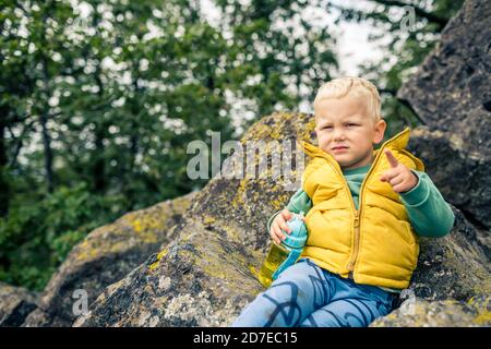 Little boy escursioni in montoni, avventura per tutta la famiglia. Piccolo bambino che cammina nella foresta rocciosa verde, sorridente. Foto Stock