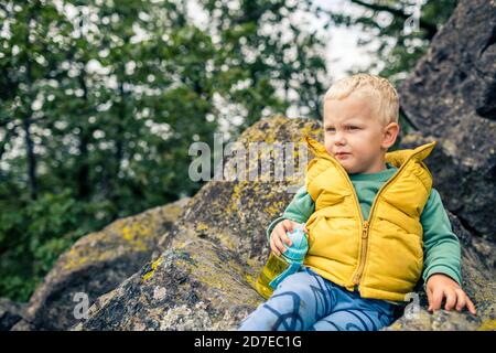 Little boy escursioni in montoni, avventura per tutta la famiglia. Piccolo bambino che cammina nella foresta rocciosa verde, sorridente. Foto Stock