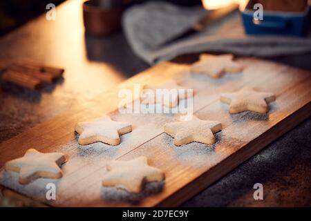 Biscotti di Natale appena sfornati a forma di stella su scheda spolverati con Zucchero a velo Foto Stock