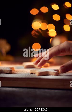 La mano delle donne raggiunge i biscotti di Natale a forma di stella appena sfornati A bordo spolverato con zucchero a velo Foto Stock