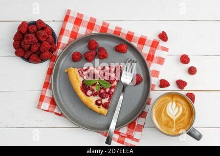 Pezzo di torta di lamponi fatta in casa con yogurt ripieno e tazza di caffè su tavolo di legno bianco. Vista dall'alto. Foto Stock