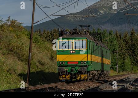 Verde treno di carico elettrico sotto le montagne di Vysoke Tatry in estate mattina soleggiata Foto Stock