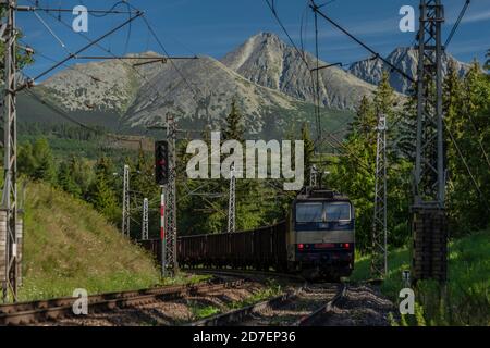 Treno elettrico blu sotto le montagne di Vysoke Tatry in estate mattina soleggiata Foto Stock