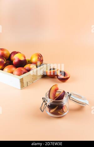 Vasetto di vetro pieno di pesche tagliate, nettarine, pesche rosse molto mature all'interno di una scatola di legno per la vendita sul retro. Sfondo color peloso Foto Stock