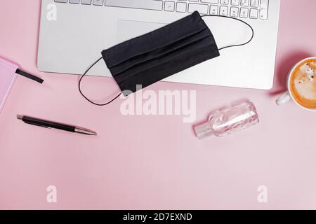 Composizione piatta con maschera medica, laptop, caffè su sfondo rosa Foto Stock