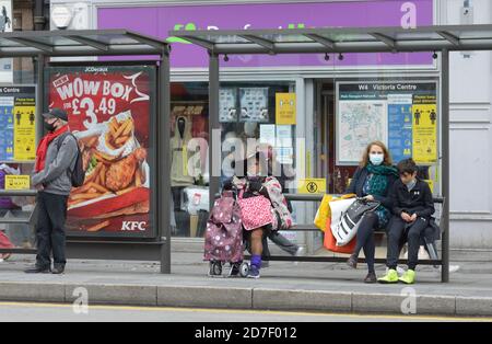 Strana signora sedette alla fermata dell'autobus, persone che indossano maschere, durante l'epidemia di Corona virus. Foto Stock