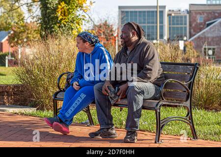 Frederick, MD, USA 10/14/2020: Una coppia interrazziale (donna caucasica e uomo afroamericano) è seduta insieme su una panchina del parco. La donna indossa Foto Stock