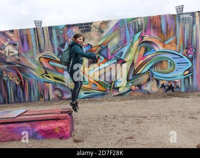 Ragazza che salta di fronte al muro di Berlino Foto Stock