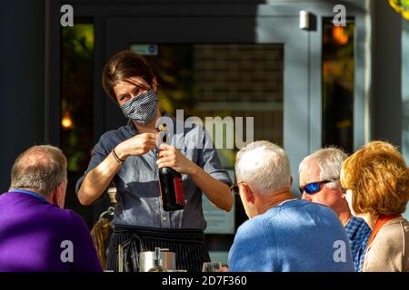 Frederick, MD, USA 10/14/2020: Una cameriera giovane che indossa una maschera facciale a causa di COVID-19 sta aprendo una bottiglia di vino per i clienti anziani che non sono in uso Foto Stock