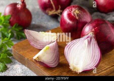 Primo piano degli cipolle viola. Cipolle porpora intere fresche e una cipolla tagliata su un piano di pietra. Foto Stock