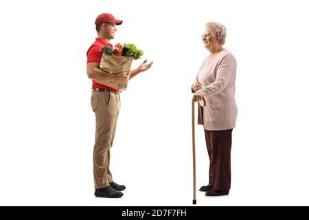 Foto di profilo a lunghezza intera di un tipo di consegna con un borsa della spesa che parla con una donna anziana isolata su bianco sfondo Foto Stock