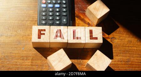 Blocchi di legno con la parola caduta e calcolatrice. Fallimento di affari e fallimento. Calo di profitto. Perdita di investimento. Crisi economica. La caduta Foto Stock