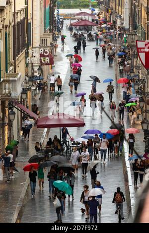Pedoni che camminano lungo corso Italia con ombrelloni in una giornata piovosa, Pisa, Toscana, Italia Foto Stock