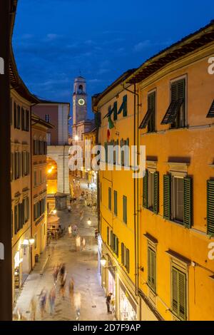 I pedoni camminano lungo corso Italia in serata, con la torre dell'orologio sullo sfondo, Pisa, Toscana, Italia Foto Stock