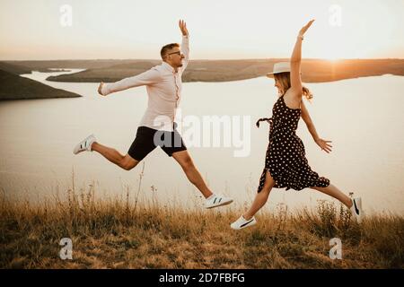 uomo e donna innamorati saltando sulla montagna sopra grande lago sul mare al tramonto Foto Stock