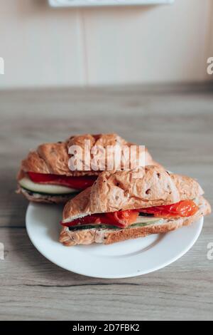 Croissant francese fresco con salmone e cetriolo su un piatto su un tavolo di legno. Delizioso concetto di cibo sano. Orientamento verticale della foto Foto Stock