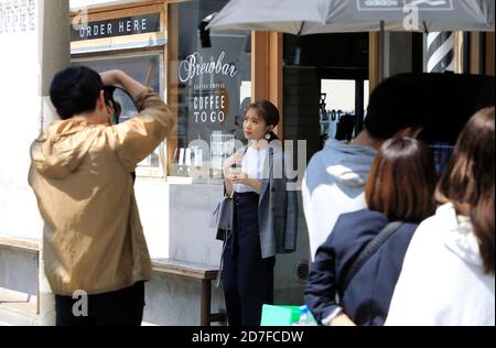 Uomo che scatta le foto di una giovane donna d'affari giapponese che tiene un Caffè all'esterno di una caffetteria locale a Ryogoku.Sumida Ku.Tokyo.Japan Foto Stock