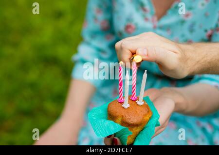 Mano con un accendisigari per illuminare i muffin al mirtillo della candela su sfondo verde. Bruciando quattro candele sulla cupcake di compleanno.celebrazione dell'anniversario. Foto Stock