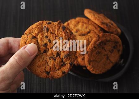Uomo che tiene in mano un biscotto con scaglie di cioccolato fatto in casa. Tasto basso. Foto Stock