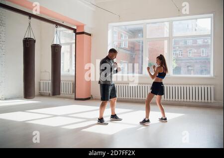 Un giovane pugile attraente insegna le sue tecniche di pugilato ragazza in un loft attrezzato per l'allenamento di pugilato Foto Stock