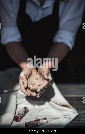 Mani bagnate ricoperte di argilla grigia di vasaio che tiene crudo pezzo di creta Foto Stock