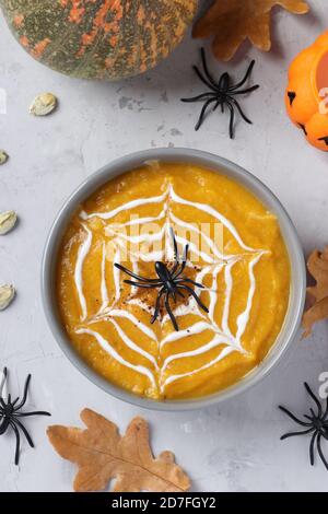 Zuppa di zucca di Halloween con ragnatela cremosa in ciotola grigia e ragni sul tavolo. Vista dall'alto. Foto Stock