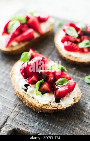 Sandwich con fragole, formaggio morbido, basilico e aceto balsamico su tavola di legno su sfondo grigio. Foto Stock