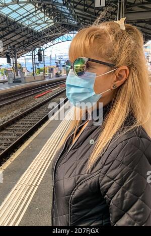 Donna adulta che indossa una maschera chirurgica presso la stazione ferroviaria. Foto Stock