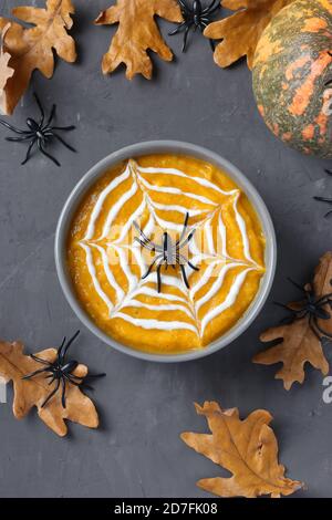 Zuppa di zucca di Halloween con ragnatela cremosa in ciotola grigia e ragni su tavola scura. Formato verticale. Foto Stock