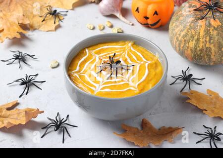 Zuppa di zucca di Halloween con ragnatela cremosa in ciotola grigia e ragni sul tavolo. Foto Stock