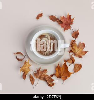 Tazza di caffè con foglie secche di autunno su sfondo biege. Vista dall'alto in piano. Foto Stock
