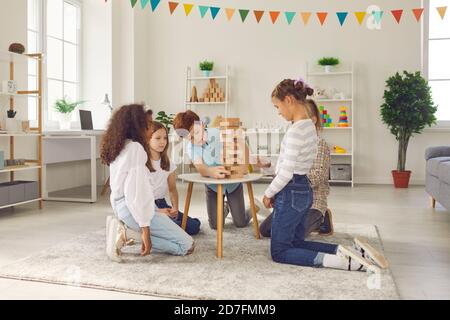 Gruppo di bambini diversi seduti a terra e gioco da tavolo con blocchi di legno a casa. Foto Stock