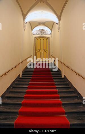 Genova - 10 ottobre 2017. Scala in pietra nera, con tappeto rosso al centro, che conduce ad una porta chiusa decorata in un antico edificio. Rotolo Foto Stock