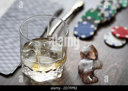 Un bicchiere di whisky e ghiaccio sul tavolo da gioco con chip e carte Foto Stock