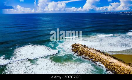 Vista aerea o foto con drone del molo roccioso o del frangiflutti nell'oceano blu. Costa da Caparica, Setubal, Almada, Portogallo Foto Stock