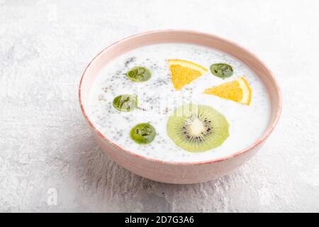 Yogurt con kiwi, uva spina, chia in ciotola di ceramica su fondo grigio di cemento. Vista laterale, primo piano. Foto Stock