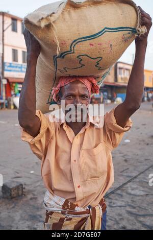 Un portatore nel Porto Vecchio di Mangalore (Mangaluru), Karnataka, India del Sud, che porta un sacco sulla sua testa lo carico su una nave Foto Stock