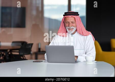 Uomo d'affari arabo sicuro e sorridente in ufficio utilizzando un computer portatile. Foto Stock
