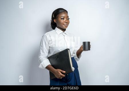 Giovane donna d'affari afroamericana sorridente e in possesso di un file e un tazza Foto Stock