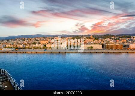 Il porto e lo skyline di Messina sull'isola di Sicilia, il principale centro turistico per le linee di crociera, sotto un cielo colorato. Foto Stock
