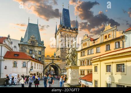 I turisti attraversano il Ponte Carlo verso la porta e la torre della città minore, mentre il sole tramonta a Praga, in Czechia. Foto Stock