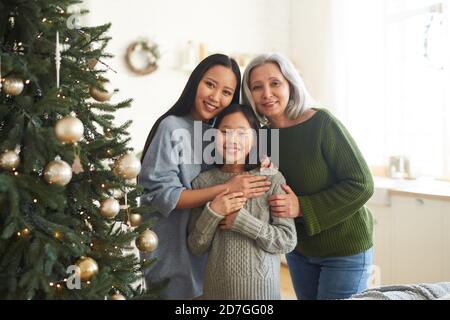 Ritratto di felice famiglia asiatica di tre sorridenti alla macchina fotografica In piedi vicino all'albero di Natale decorato a casa Foto Stock