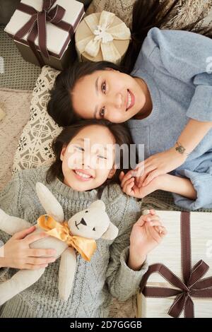 Vista ad alto angolo della madre asiatica che gioca con sua figlia con il giocattolo che giace sul pavimento a casa Foto Stock
