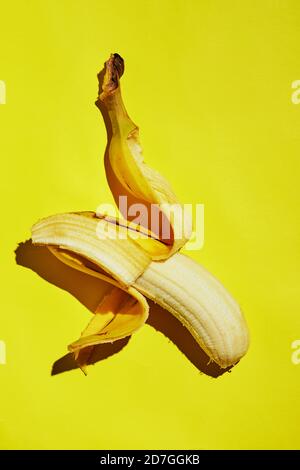 Banana a mezza buccia isolata su fondo a gradiente giallo. Foto Stock