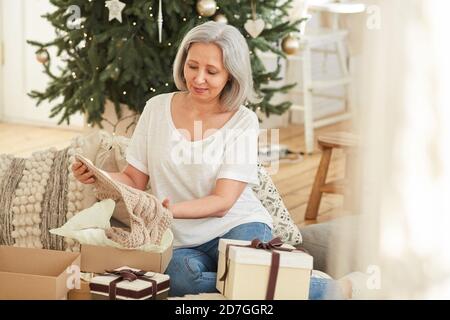 Donna matura che apre il regalo di Natale e che ottiene la sciarpa calda senza confezione Foto Stock