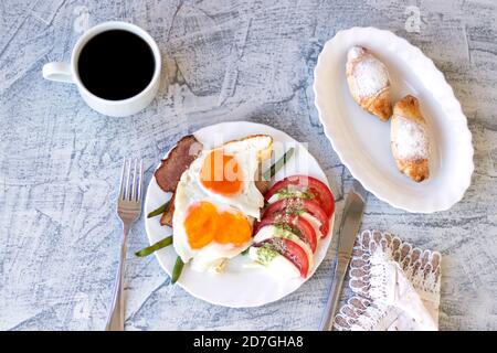 Colazione italiana con caffè e caprese. Uova fritte con pancetta, pomodori, mozzarella, fagioli verdi e croissant. Deliziosa colazione servita su tavolo testurizzato con tovagliolo. Vista dall'alto. Messa a fuoco morbida Foto Stock