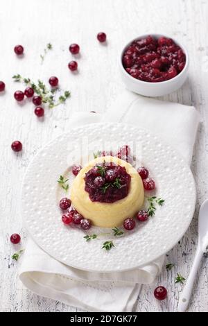 Cheesecake, budino di formaggio con marmellata di mirtilli rossi, mirtilli freschi e timo su un piatto bianco su un vecchio sfondo bianco, fuoco selettivo Foto Stock