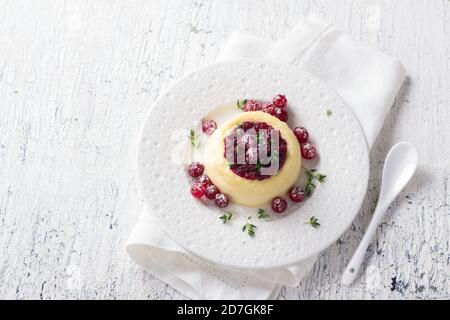 Cheesecake, budino di formaggio con marmellata di mirtilli rossi, mirtilli freschi e timo su un piatto bianco su un vecchio sfondo bianco, fuoco selettivo Foto Stock