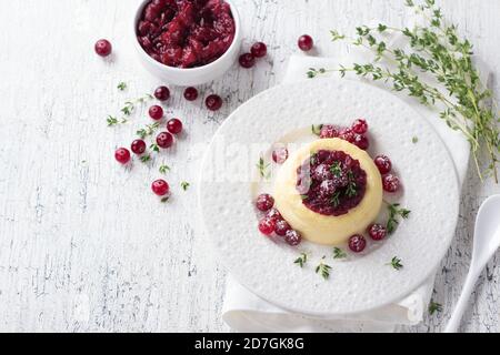 Cheesecake, budino di formaggio con marmellata di mirtilli rossi, mirtilli freschi e timo su un piatto bianco su un vecchio sfondo bianco, fuoco selettivo Foto Stock